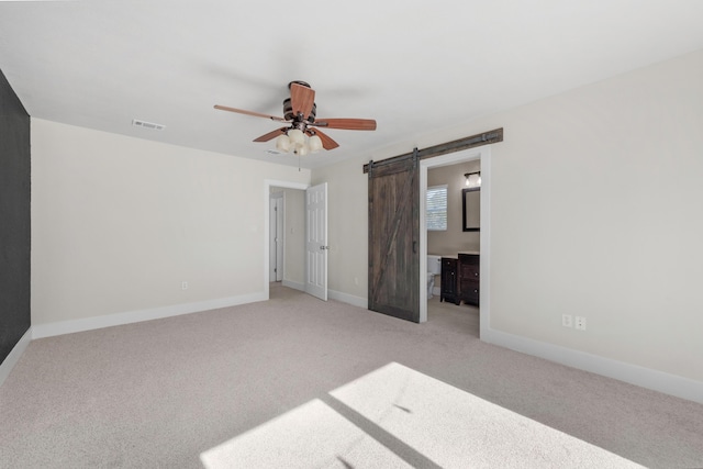 unfurnished bedroom featuring a barn door, ceiling fan, ensuite bathroom, and light carpet