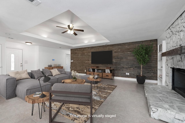 living room featuring a raised ceiling, a stone fireplace, and ceiling fan