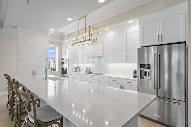 kitchen with appliances with stainless steel finishes, custom range hood, sink, white cabinetry, and hanging light fixtures