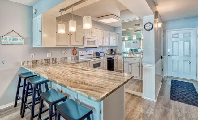 kitchen featuring kitchen peninsula, a kitchen breakfast bar, white appliances, pendant lighting, and light hardwood / wood-style floors