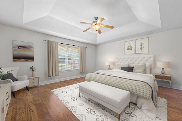 bedroom with ceiling fan, a raised ceiling, and dark wood-type flooring