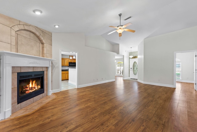 unfurnished living room with a tiled fireplace, ceiling fan, light hardwood / wood-style flooring, and high vaulted ceiling