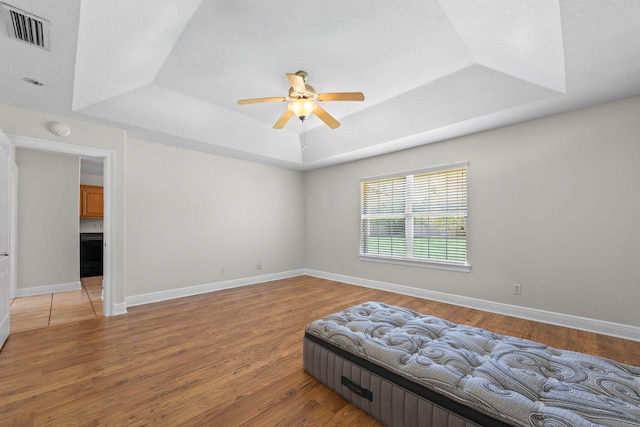 bedroom with a raised ceiling, a textured ceiling, light hardwood / wood-style flooring, and ceiling fan
