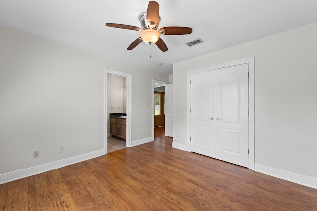 unfurnished bedroom featuring ceiling fan, light hardwood / wood-style floors, a closet, and ensuite bath
