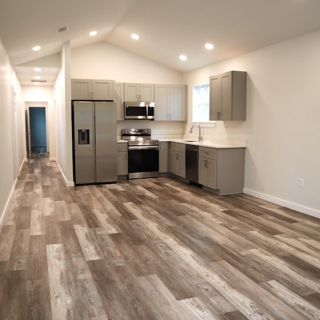 kitchen featuring sink, dark hardwood / wood-style flooring, lofted ceiling, gray cabinets, and appliances with stainless steel finishes