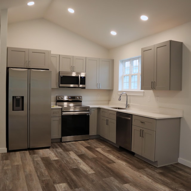 kitchen with appliances with stainless steel finishes, gray cabinets, vaulted ceiling, and dark wood-type flooring