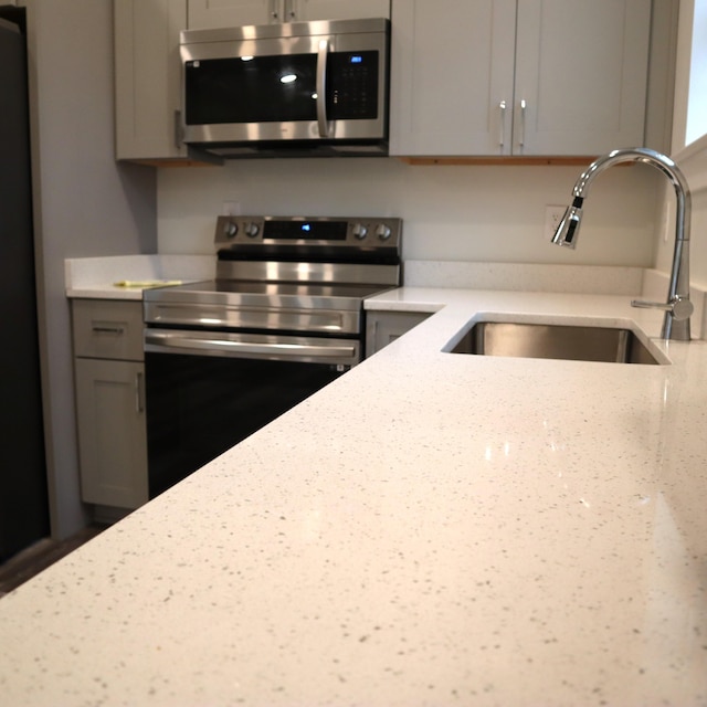 kitchen featuring stainless steel appliances, light stone counters, gray cabinetry, and sink