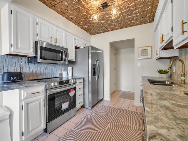 kitchen featuring light stone countertops, stainless steel appliances, sink, light tile patterned floors, and white cabinetry