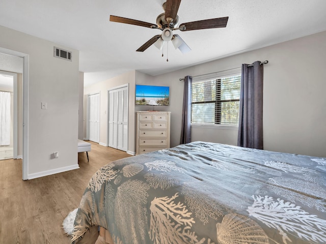 bedroom featuring ceiling fan, hardwood / wood-style floors, and two closets