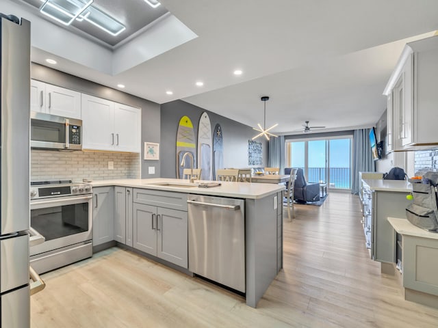 kitchen featuring kitchen peninsula, ceiling fan, light hardwood / wood-style floors, and appliances with stainless steel finishes