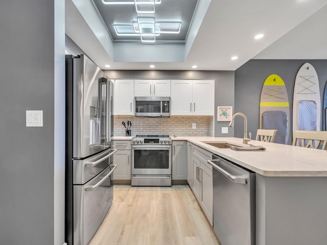 kitchen with sink, appliances with stainless steel finishes, light hardwood / wood-style floors, a kitchen bar, and kitchen peninsula