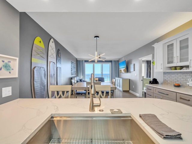 kitchen with backsplash, white cabinets, decorative light fixtures, a notable chandelier, and wood-type flooring