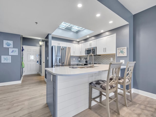 kitchen with white cabinetry, backsplash, light hardwood / wood-style floors, a breakfast bar area, and appliances with stainless steel finishes