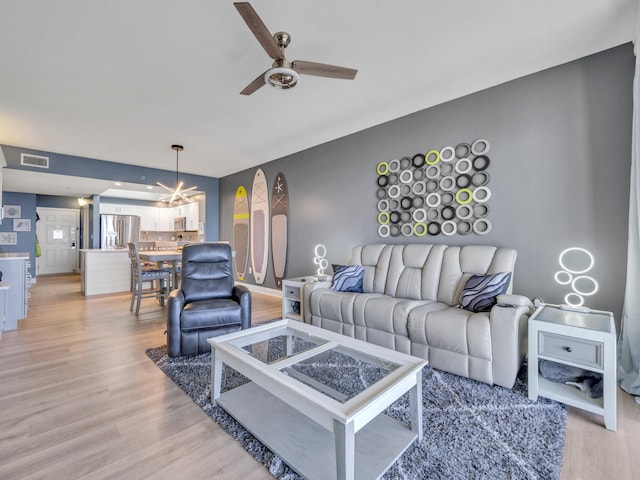 living room featuring ceiling fan with notable chandelier and light wood-type flooring