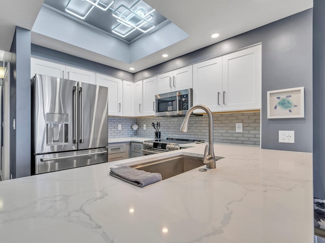 kitchen featuring appliances with stainless steel finishes, backsplash, white cabinetry, and light stone counters