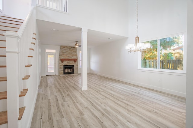 unfurnished living room with a high ceiling, ceiling fan with notable chandelier, light hardwood / wood-style flooring, and a stone fireplace