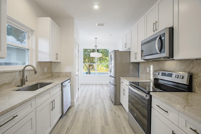 kitchen with sink, stainless steel appliances, light hardwood / wood-style flooring, pendant lighting, and white cabinets