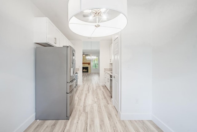 interior space featuring white cabinets, ceiling fan, stainless steel fridge, light wood-type flooring, and a fireplace