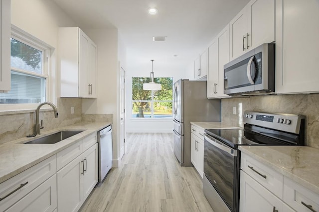 kitchen with backsplash, white cabinets, appliances with stainless steel finishes, decorative light fixtures, and light hardwood / wood-style floors