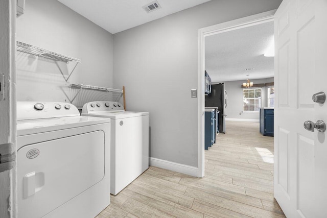 clothes washing area featuring a textured ceiling, light hardwood / wood-style floors, an inviting chandelier, and washing machine and clothes dryer