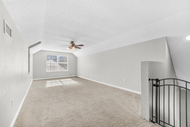 additional living space with a textured ceiling, ceiling fan, light colored carpet, and vaulted ceiling