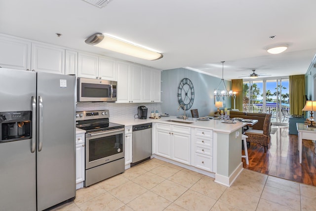 kitchen featuring sink, kitchen peninsula, white cabinets, ceiling fan with notable chandelier, and appliances with stainless steel finishes