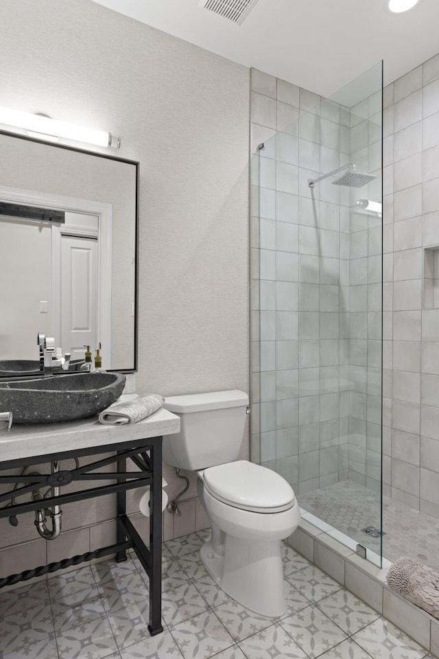 bathroom with a tile shower, sink, and toilet