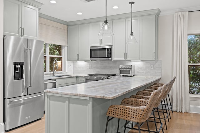 kitchen with light stone countertops, sink, hanging light fixtures, stainless steel appliances, and light hardwood / wood-style flooring