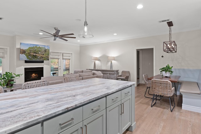 kitchen featuring light stone countertops, light wood-type flooring, hanging light fixtures, and ornamental molding