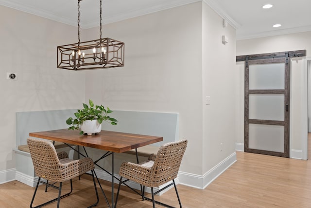 dining space with a barn door, light hardwood / wood-style flooring, crown molding, and a notable chandelier