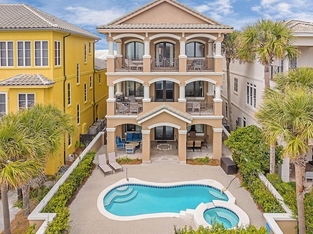 rear view of property featuring a pool with hot tub, a balcony, and a patio