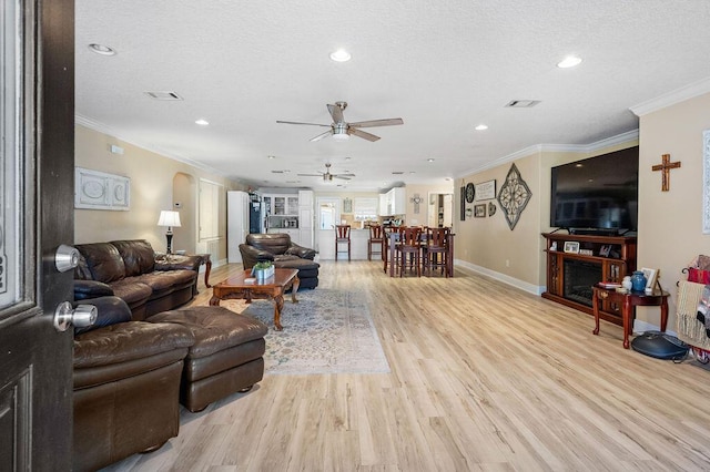 living room featuring ceiling fan, light hardwood / wood-style floors, ornamental molding, and a textured ceiling