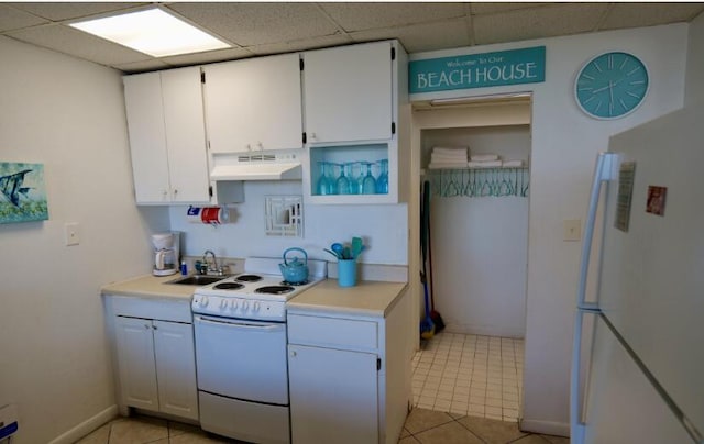 kitchen with a paneled ceiling, white appliances, sink, white cabinets, and light tile patterned flooring