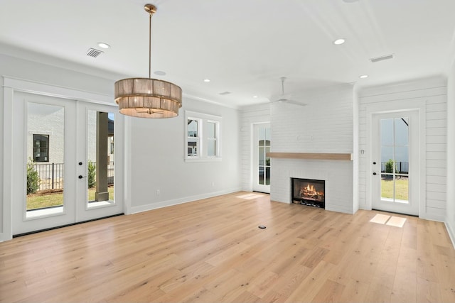 unfurnished living room featuring ceiling fan, a large fireplace, light wood-type flooring, and french doors