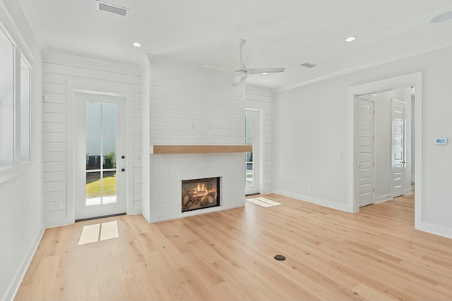 unfurnished living room featuring ceiling fan, light wood-type flooring, ornamental molding, and a brick fireplace