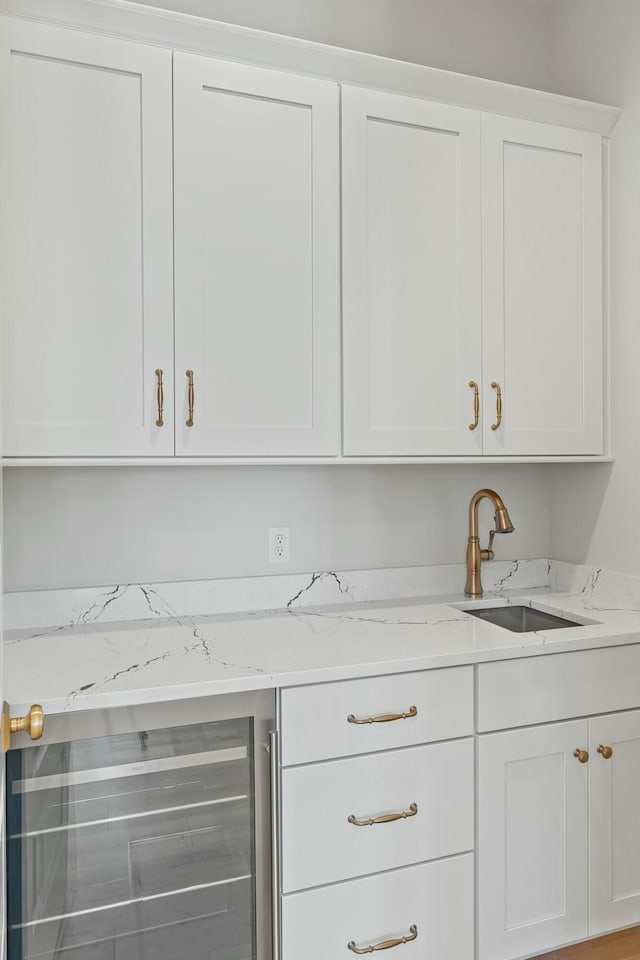 bar with white cabinetry, sink, beverage cooler, and light stone counters