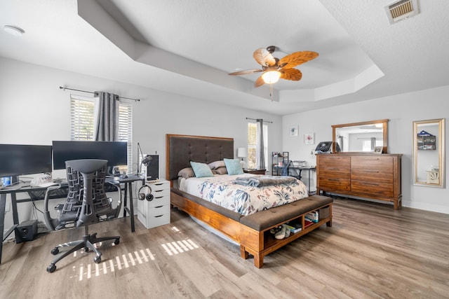 bedroom with hardwood / wood-style floors, ceiling fan, a tray ceiling, and multiple windows