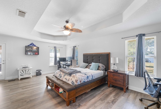 bedroom with a raised ceiling, ceiling fan, a textured ceiling, and hardwood / wood-style flooring