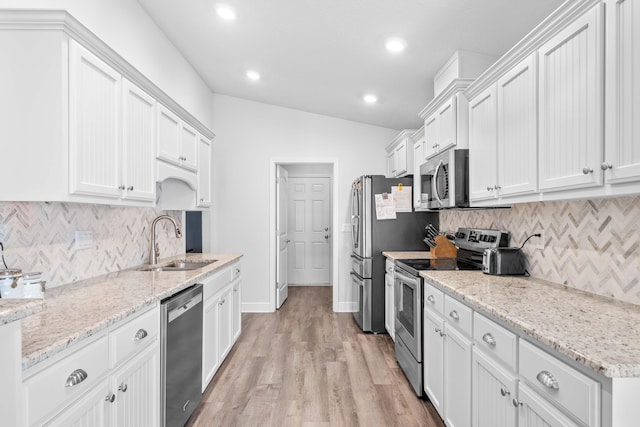 kitchen with appliances with stainless steel finishes, light wood-type flooring, sink, white cabinets, and lofted ceiling