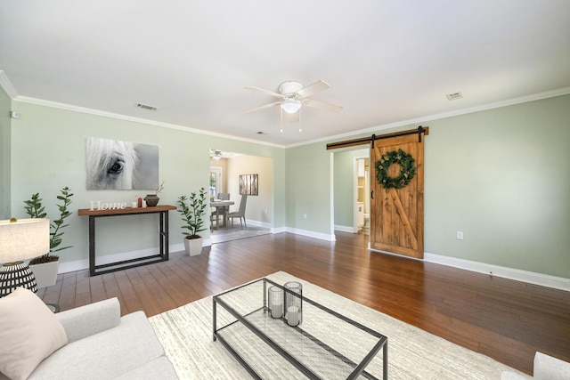 living area featuring visible vents, a barn door, hardwood / wood-style flooring, and a ceiling fan