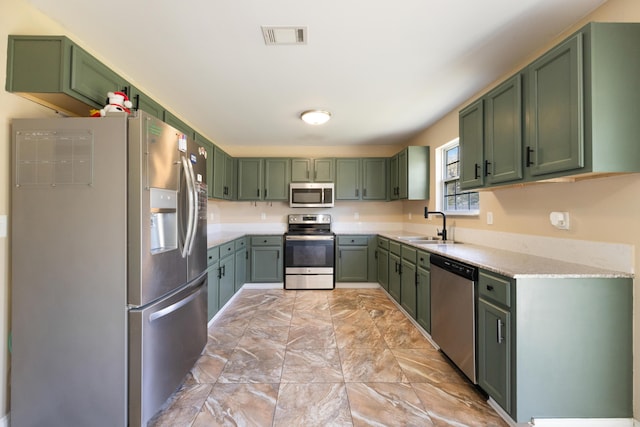 kitchen featuring visible vents, light stone countertops, stainless steel appliances, a sink, and green cabinetry