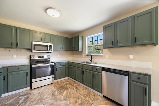 kitchen with green cabinets, light stone countertops, a sink, and stainless steel appliances