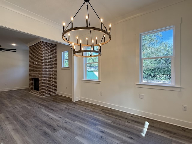 unfurnished dining area featuring a fireplace, baseboards, a chandelier, and dark wood-style flooring