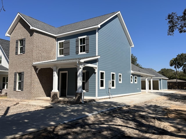 view of front of property featuring driveway, covered porch, a shingled roof, and brick siding