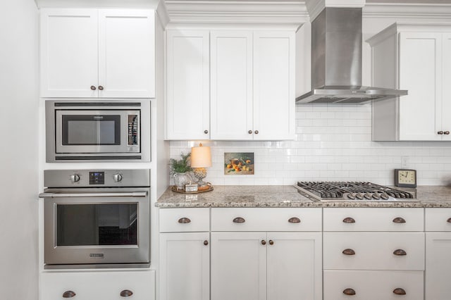 kitchen with backsplash, stainless steel appliances, white cabinetry, and wall chimney range hood