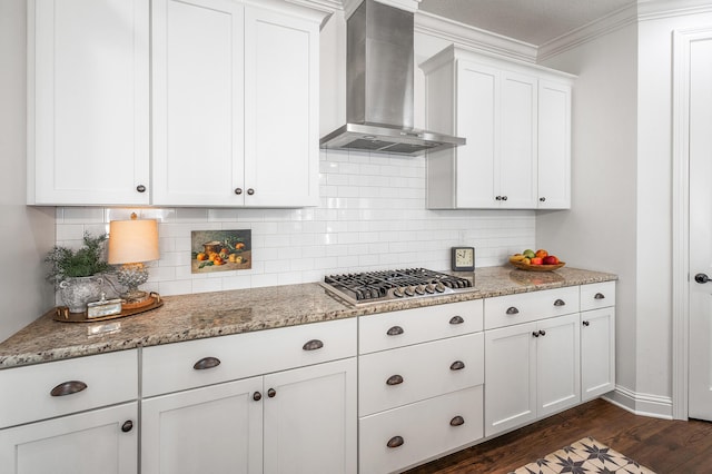 kitchen with light stone counters, ornamental molding, wall chimney range hood, white cabinets, and stainless steel gas stovetop