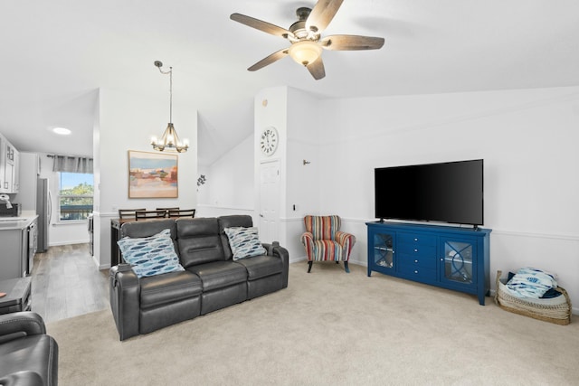 living room with ceiling fan with notable chandelier, light colored carpet, and vaulted ceiling