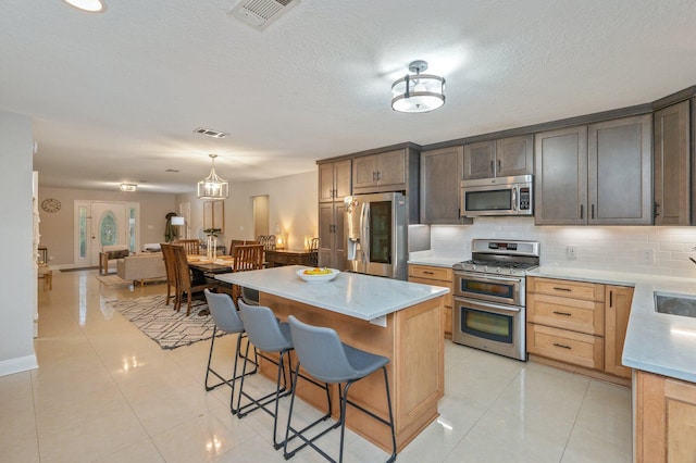 kitchen featuring stainless steel appliances, pendant lighting, a kitchen island, light tile patterned flooring, and tasteful backsplash