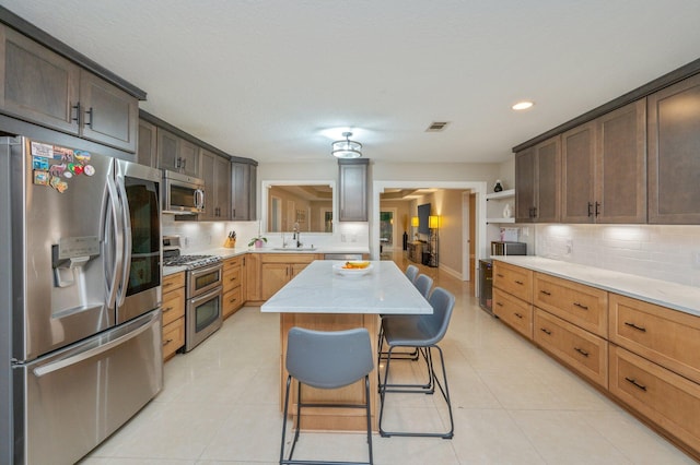 kitchen featuring a breakfast bar area, stainless steel appliances, a kitchen island, decorative backsplash, and sink