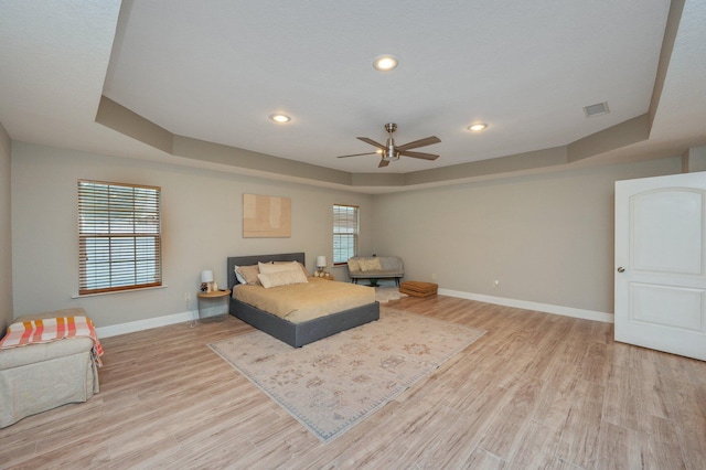 bedroom with ceiling fan, light wood-type flooring, and a tray ceiling